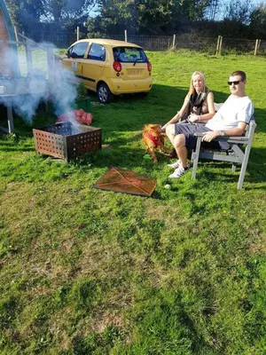a man and woman sitting on a bench next to a fire at Cozy Cabin Retreat in Saint Austell in Lanivet
