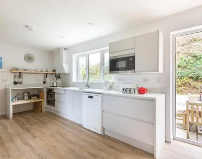a kitchen with white cabinets and a large window at Beaches in Polzeath