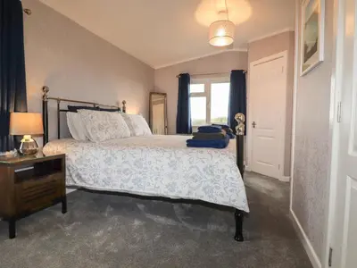 a bedroom with a bed and a dresser and a window at Sycamore Lodge in Helston