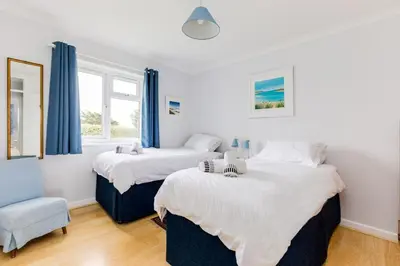 two beds in a room with blue curtains and a chair at Trebartha in Polzeath