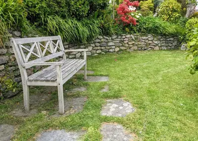 a wooden bench sitting in the grass near a stone wall at Seaside Holiday Cottage Near Beach in Charlestown