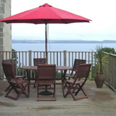 a table and chairs with a red umbrella on a patio at Seaside Holiday Cottage Near Beach in Charlestown