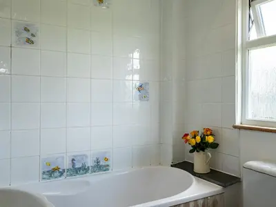 a white bathroom with a tub and a vase of flowers at Atlantic Lodge in Port Isaac