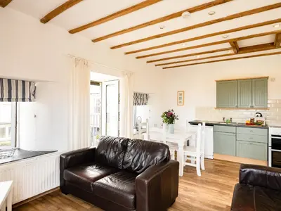 a living room with a leather couch and a kitchen at Swallow Cottage, Trewetha Farm in Port Isaac