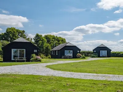 two black cottages in a field with a gravel driveway at Harbour Lodge in Port Isaac