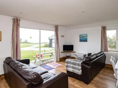 a living room with leather furniture and a large window at Campion Lodge in Port Isaac