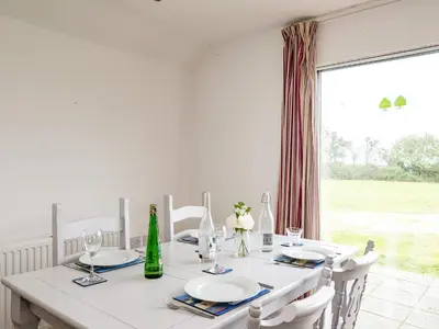 a white dining room with a table and a large window at Puffin Lodge in Port Isaac