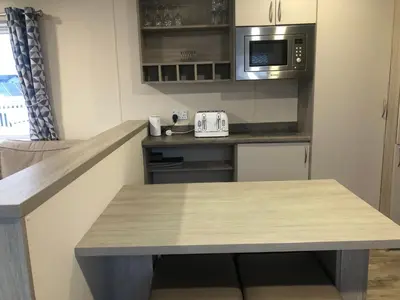 a kitchen with a table and a microwave at Luxury 3 bedroom caravan between Perranporth and Newquay, Cornwall in Newquay