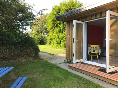 a small cabin with a table and a yellow chair on the porch at Woodpecker Glamping Cabin in Bodmin