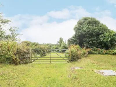 an open gate in a grassy field with trees at South Boduel Farmhouse in Liskeard