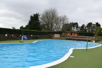 a large blue swimming pool with a house in the background at Contemporary Caravan at Newquay Holiday Park in Newquay