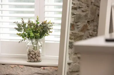 a vase filled with rocks and flowers in a window at Beach Cottage and The Lobster Pot in St. Agnes