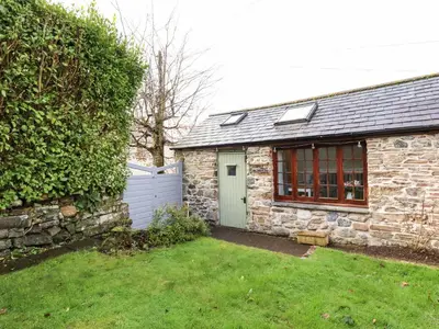 a stone house with a fence and a yard at Little Orchard Barn in St Austell