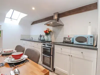a kitchen with white cabinets and a wooden table at Water WheelsThe West Dry in St Austell