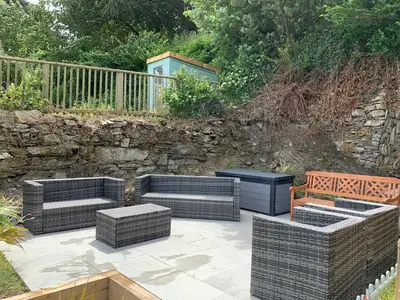 a patio with three wicker furniture and a stone wall at The Slipway Fowey Harbour Parking 1 Min & Garden in Fowey