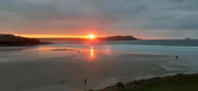 a sunset on a beach with people in the water at Trewethen Cottage Barn 2 near Port Isaac in Port Isaac