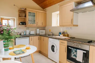 a kitchen with wooden cabinets and a white dishwasher at Kitts Cottage, Redruth, Cosy Cornish Retreat in Redruth
