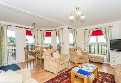 a living room with a table and chairs and a television at Wendy Lodge- Chalet Cottage, Sleeps 6 Adults in Padstow