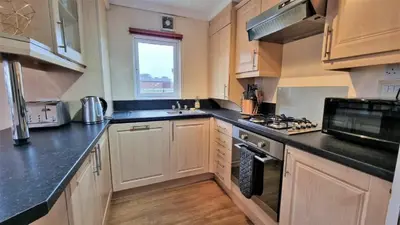 a kitchen with wooden cabinets and black counter tops at Wendy Lodge- Chalet Cottage, Sleeps 6 Adults in Padstow