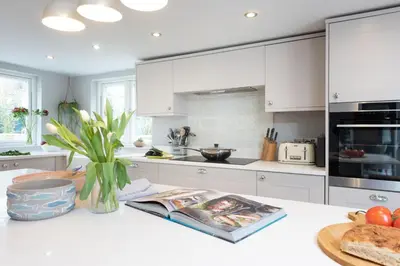 a kitchen with white cabinets and a vase of flowers on a counter at Beach Cottage in St. Agnes