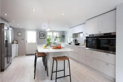 a kitchen with white cabinets and a kitchen island with stools at Beach Cottage in St. Agnes