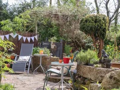 a patio with a table and chairs in a garden at The Nest in Helston