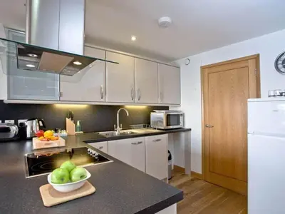 a kitchen with white cabinets and a bowl of fruit on a counter at Sunset Surf - Mount Brioni in Downderry