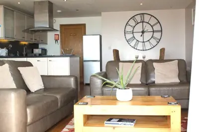 a living room with two brown couches and a clock on the wall at Sunset Surf - Mount Brioni in Downderry