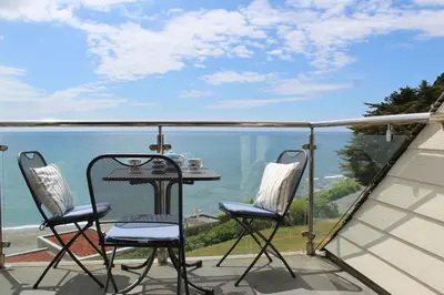 a balcony with two chairs and a table and the ocean at Seascape - Mount Brioni in Downderry