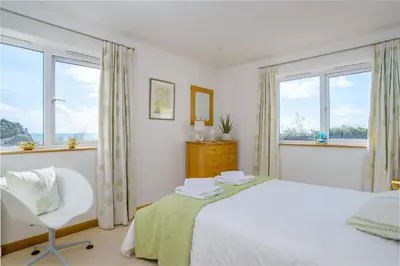 a bedroom with a bed and a chair and windows at Lowena - Mount Brioni in Downderry