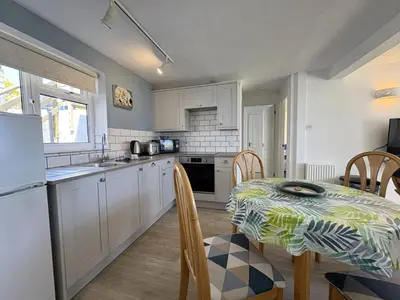 a kitchen with a table and a kitchen with white cabinets at Surf Watch - Mount Brioni in Downderry