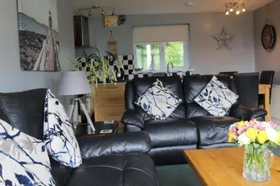 a living room with a black leather couch and a table at Cornish Riviera - Mount Brioni in Downderry