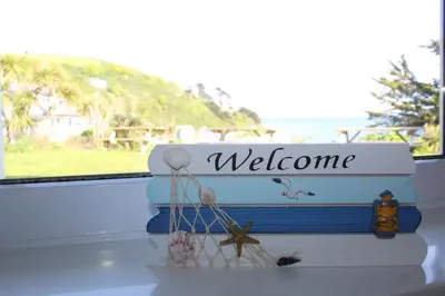 a bench with a welcome sign and a window at Salty Air - Mount Brioni in Downderry