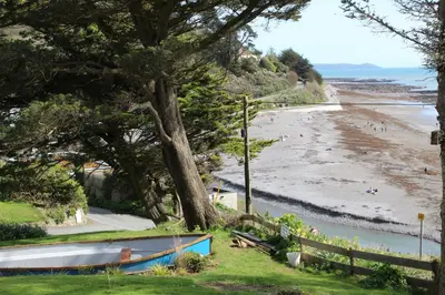 a beach with a tree and a boat on the grass at Salty Air - Mount Brioni in Downderry