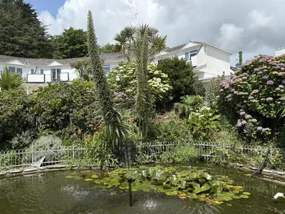 a garden with a pond with flowers and plants at Sea Breeze - Mount Brioni in Downderry
