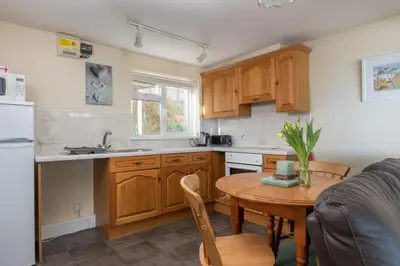 a kitchen with wooden cabinets and a wooden table with a dining room at Sand Bar - Mount Brioni in Downderry