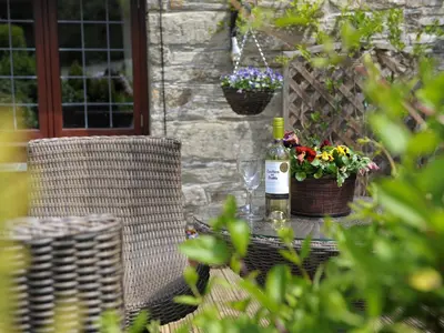 a table with a bottle of wine and a basket of flowers at Nightingale Cottage in Liskeard