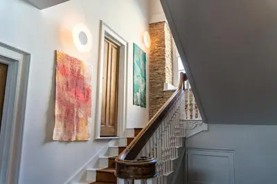a hallway with stairs with paintings on the walls at Finest Retreats - ARC Padstow in Little Petherick