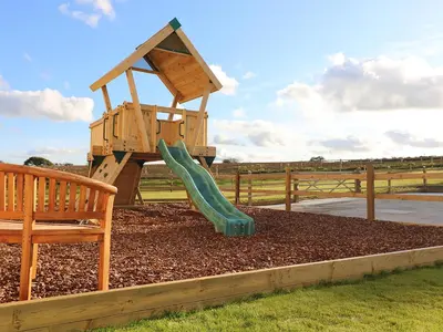 a wooden playground with a slide and a bench at The Granary at Boskensoe Barns in Falmouth