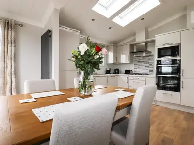 a kitchen with a wooden table with chairs and a vase of flowers at Acorn Lodge in Redruth