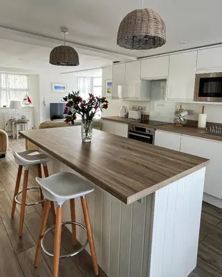 a kitchen with a large wooden counter with two stools at Cliff House - a stunning sea view 2 bed apartment in Porthleven in Porthleven
