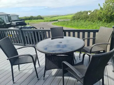 a table and chairs on a deck with a view of a road at Mawgan Pads Perranporth in Cubert