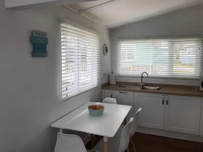 a kitchen with a white table and chairs and windows at Holiday Chalet at Gwithian Sands in Cornwall in Gwithian