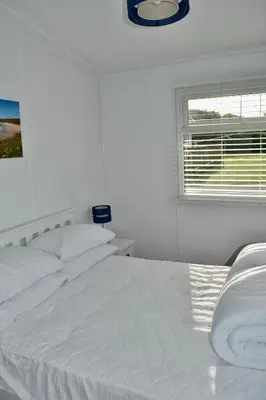 a white bed in a white bedroom with a window at Holiday Chalet at Gwithian Sands in Cornwall in Gwithian