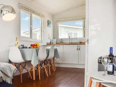 a kitchen with white cabinets and a table with chairs at Holiday Chalet at Gwithian Sands in Cornwall in Gwithian