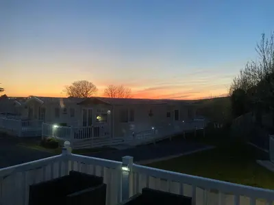a house with a fence in front of a sunset at Mollys Retreat pet friendly three bed caravan with small garden Newquay Bay Resort Quieter area of park in Newquay