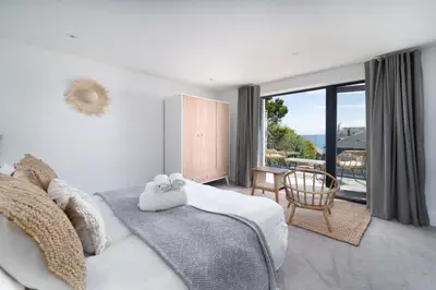a white bedroom with a bed and a balcony at Del Mar in St Ives