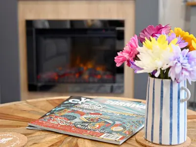 a vase of flowers on a table next to a magazine at Rose View in Newquay