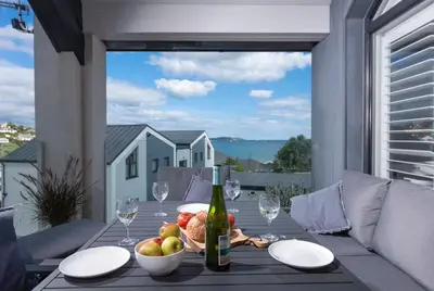 a table with a bowl of fruit and a bottle of wine at Swanpool View - Walk to Beach - Free WiFi & Parking - Sea & Lake Views in Falmouth