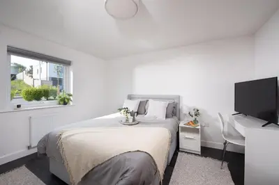 a white bedroom with a bed and a flat screen tv at Swanpool View - Walk to Beach - Free WiFi & Parking - Sea & Lake Views in Falmouth